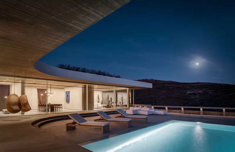 Illuminated pool and terrace with glazed living pavilion under timber soffit at night with full moon