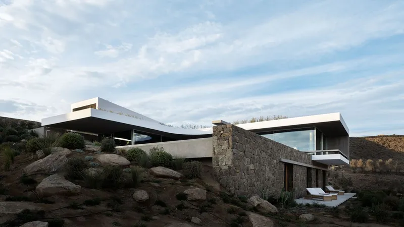 Stacked volumes with stone retaining walls and cantilevered roof planes amid boulders and native grasses
