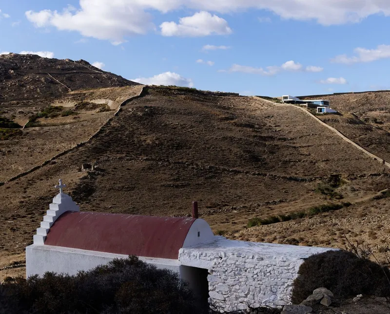 White chapel with burgundy barrel vault and stepped bell tower in a rugged hillside setting