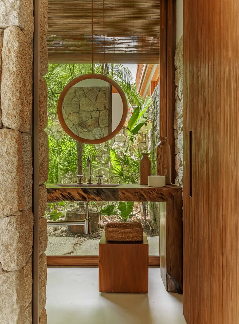 Bathroom vanity with circular mirror framed by stone walls and view to planted courtyard beyond