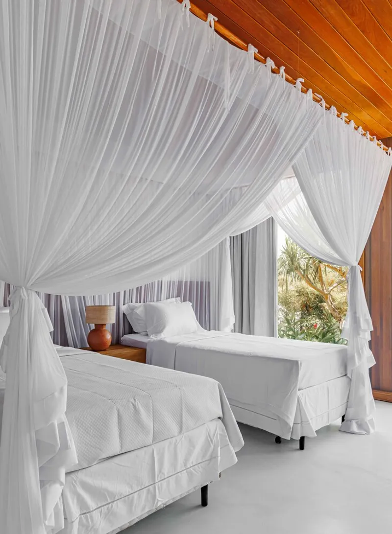 Twin beds under mosquito netting with a curved timber ceiling soffit and garden view