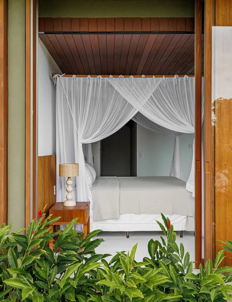 Bedroom entry framed by timber sliding doors with white canopy curtains and tropical plantings in foreground