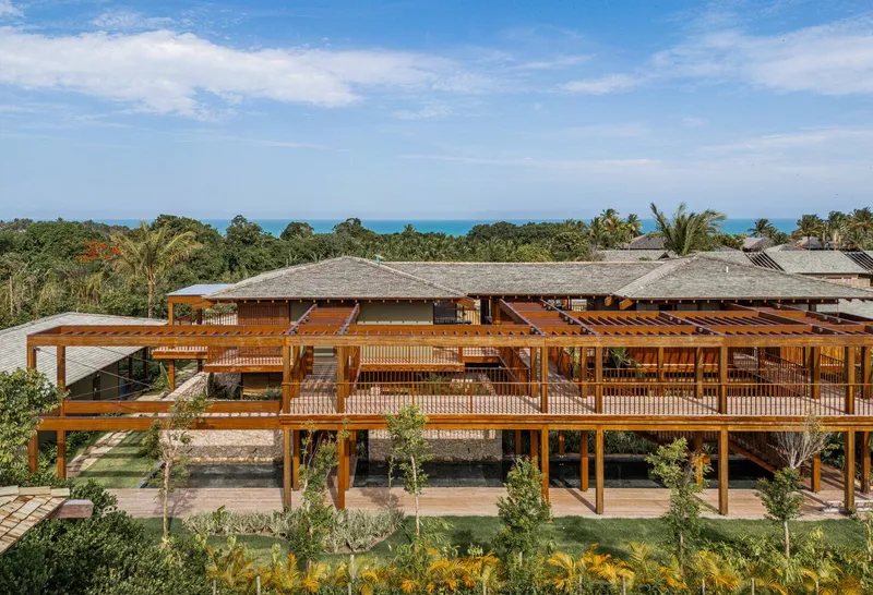 Elevated timber structure with hipped roofs and open walkways above lawn and tropical vegetation under blue sky