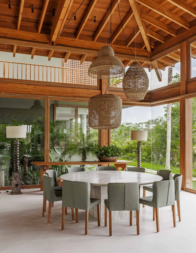 Dining area beneath pitched timber roof with lattice screen at upper gallery and woven pendant fixtures