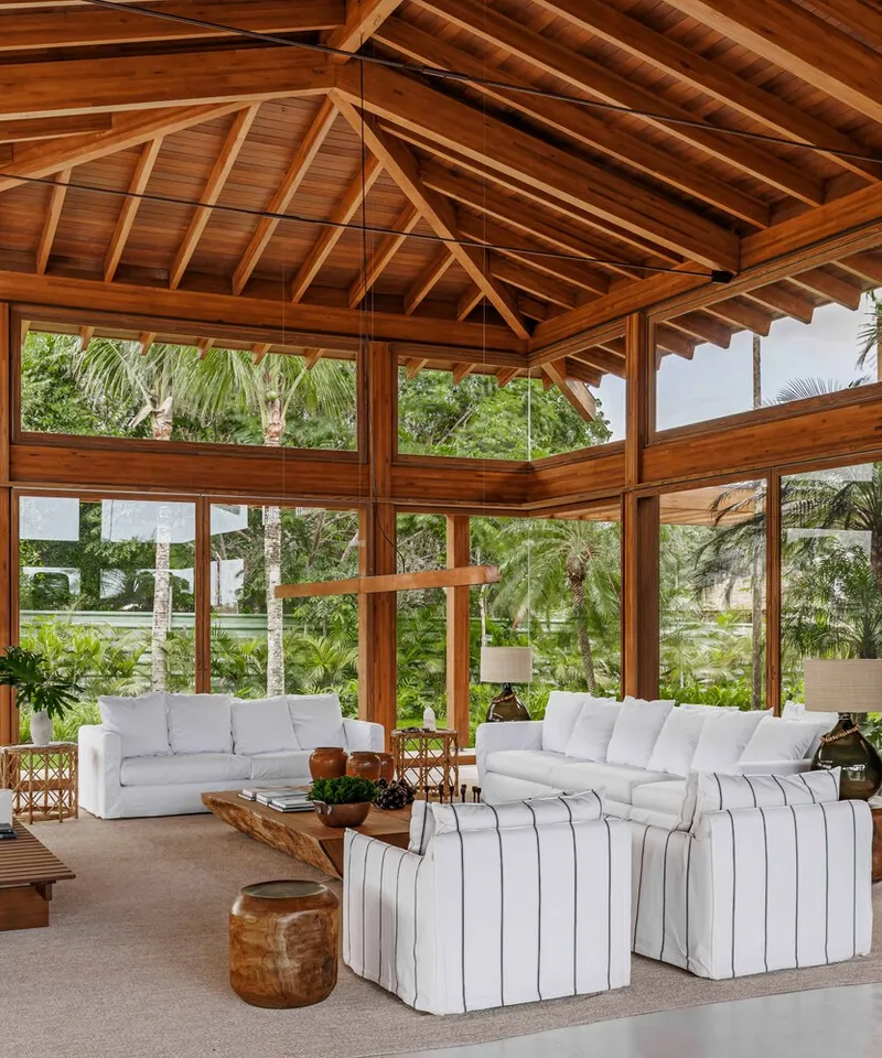Timber-framed pavilion with exposed rafter ceiling and full-height glazing overlooking palm trees