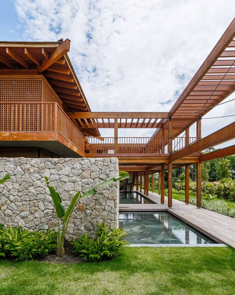 Stone wall base supporting timber bridge and balcony structure above reflecting pool and lawn