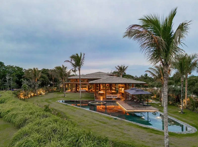 Evening view of the timber pavilion and pool terrace surrounded by palm trees and tropical vegetation