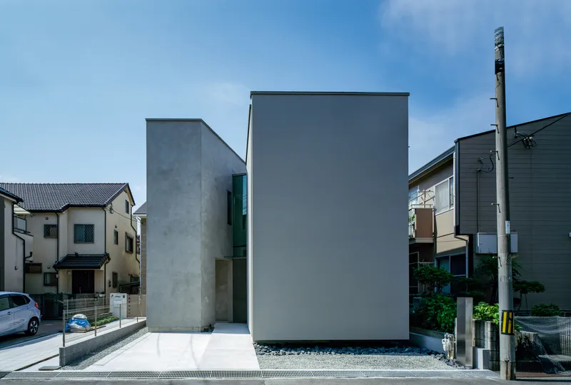 Street view of two concrete volumes with a glazed recess between neighboring houses