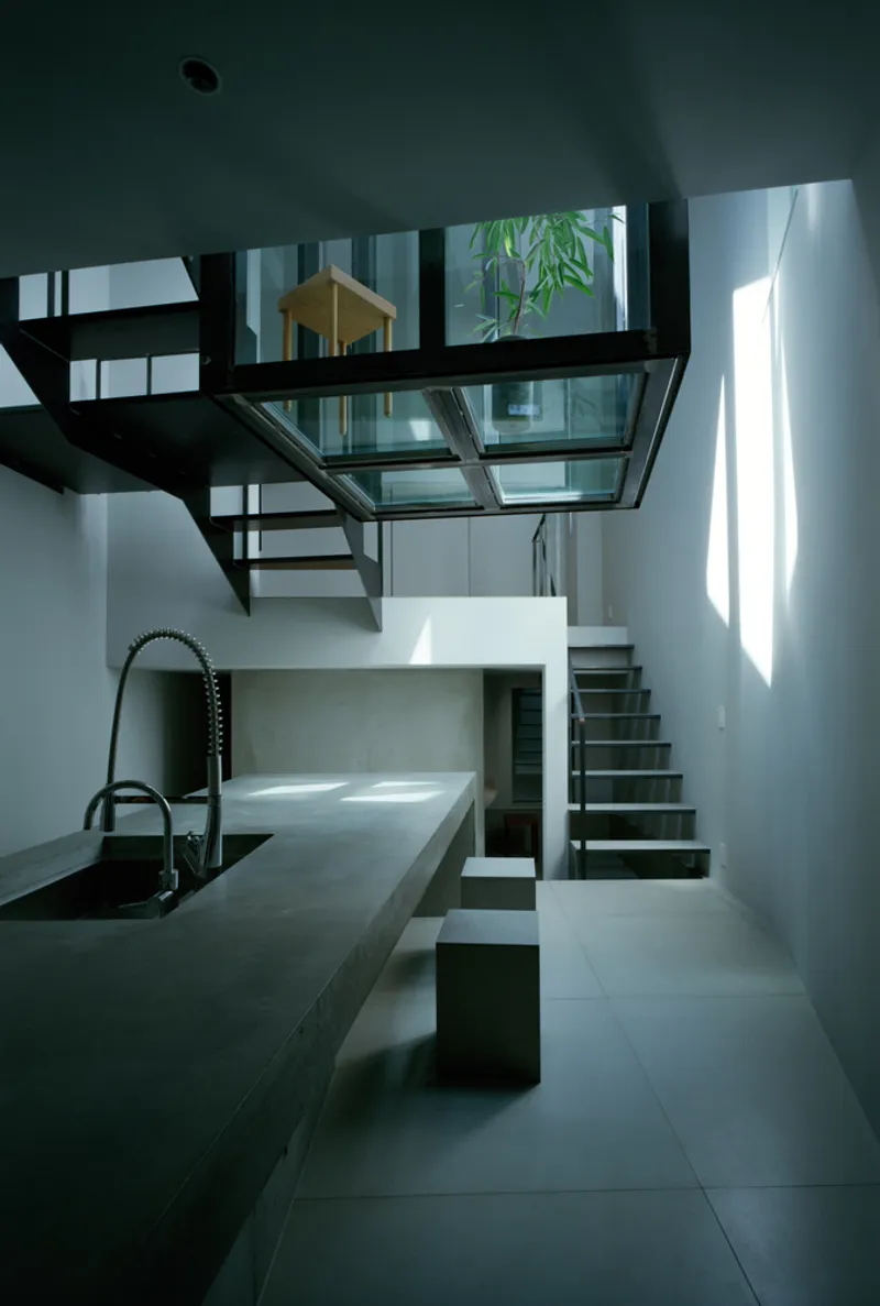 Steel and glass staircase rising to a skylight with bamboo visible in courtyard above