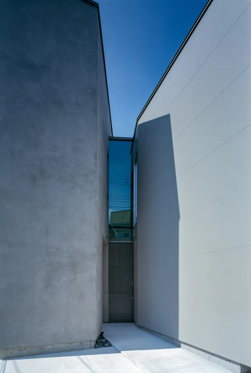 Narrow exterior passage between two concrete walls open to blue sky above