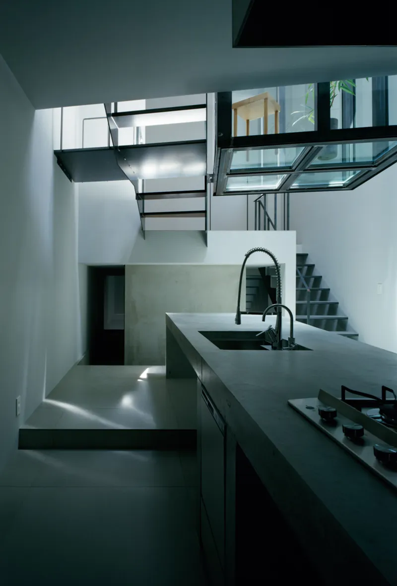 Double-height kitchen space with suspended steel staircase and glass floor bridge illuminated by skylights