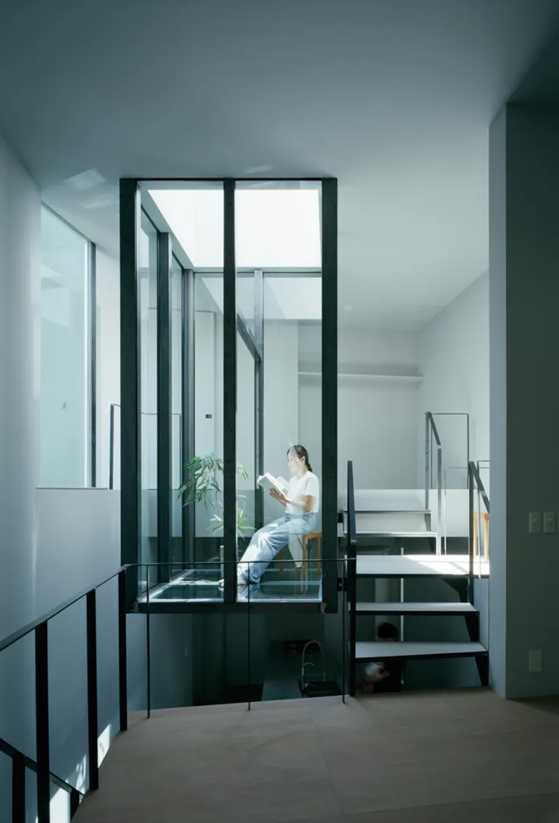 Glass-enclosed reading nook with steel staircase and person seated with greenery inside