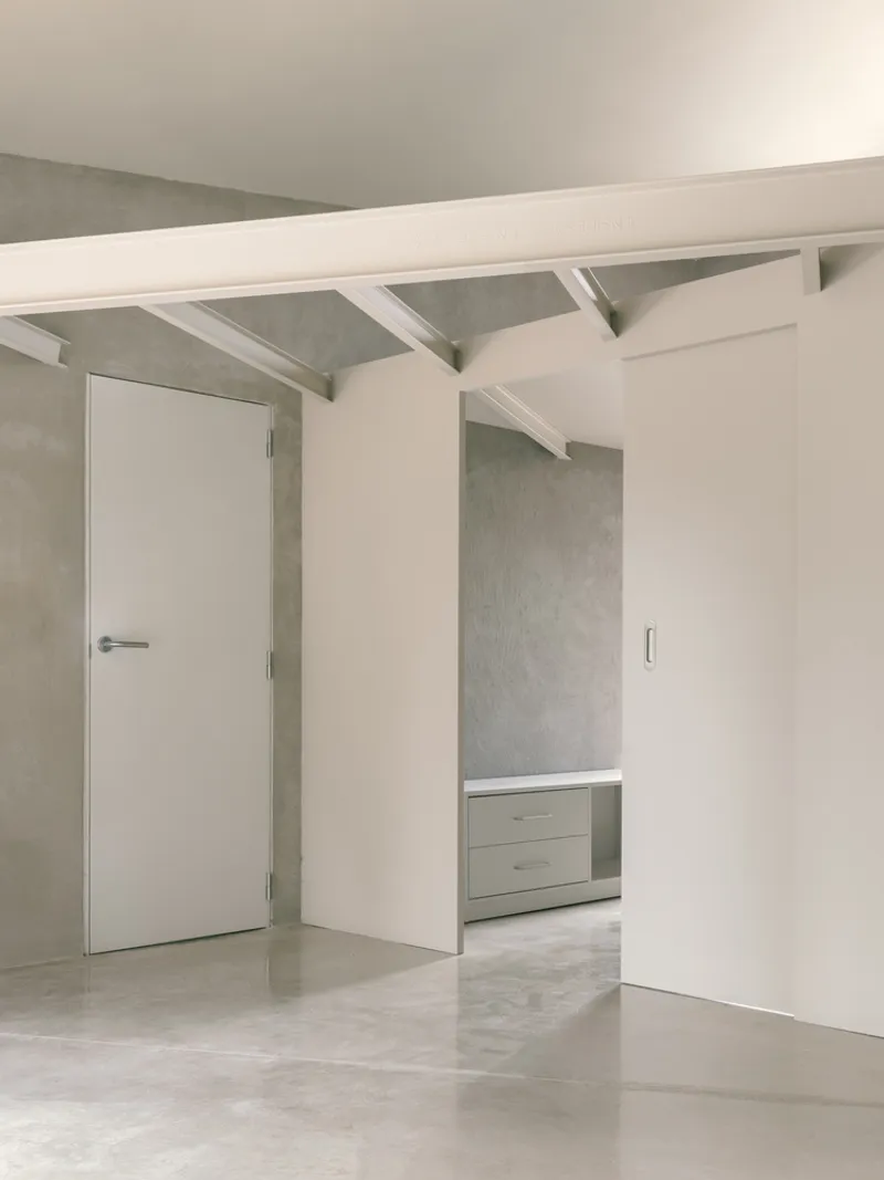 Interior hallway with white door, exposed rafters, and polished concrete flooring in soft daylight