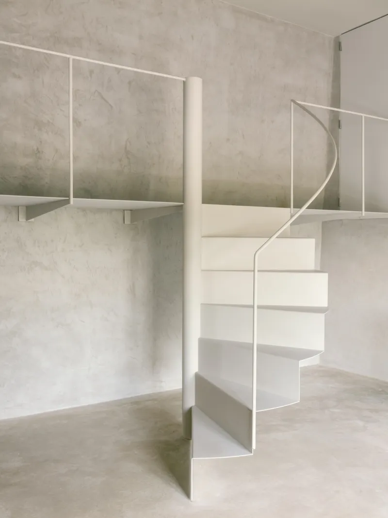 White metal spiral staircase with mezzanine railing against textured grey plaster wall