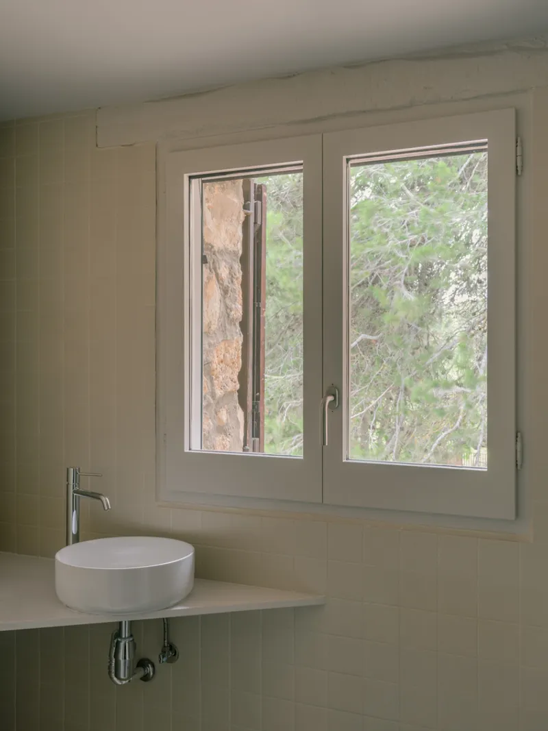 Bathroom sink detail with window framing stone wall and tree branches beyond