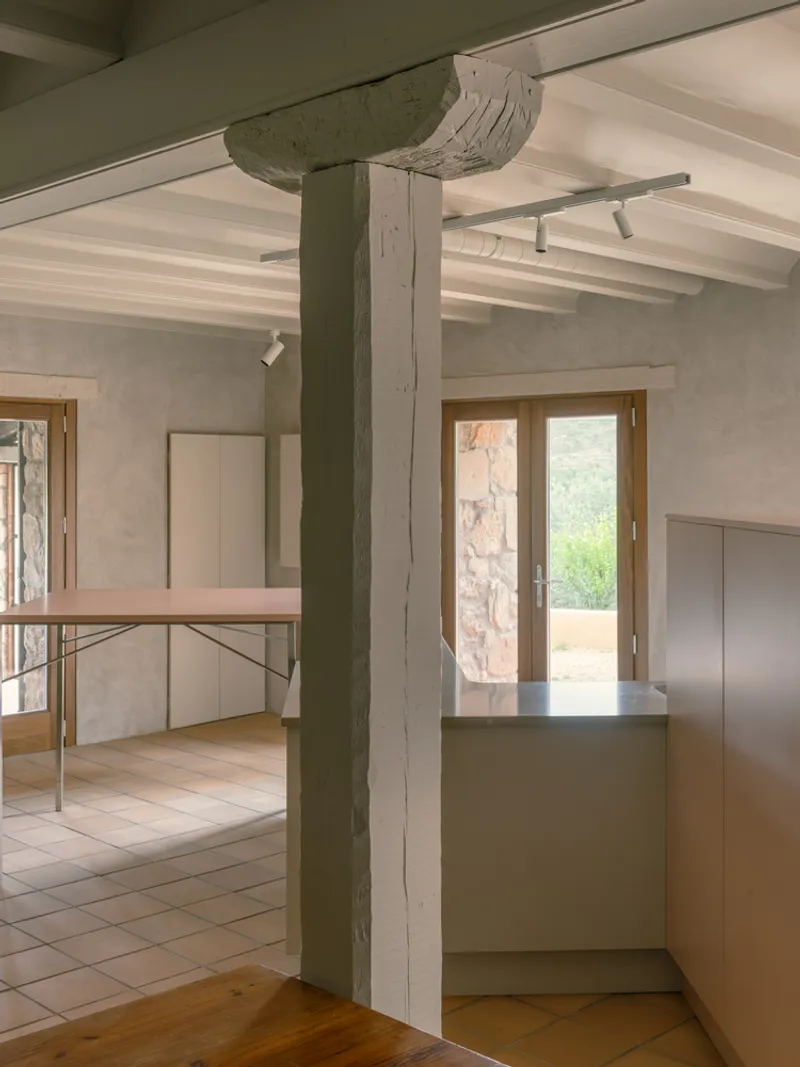 View past painted timber column showing pink table, kitchen counter, and exposed ceiling beams