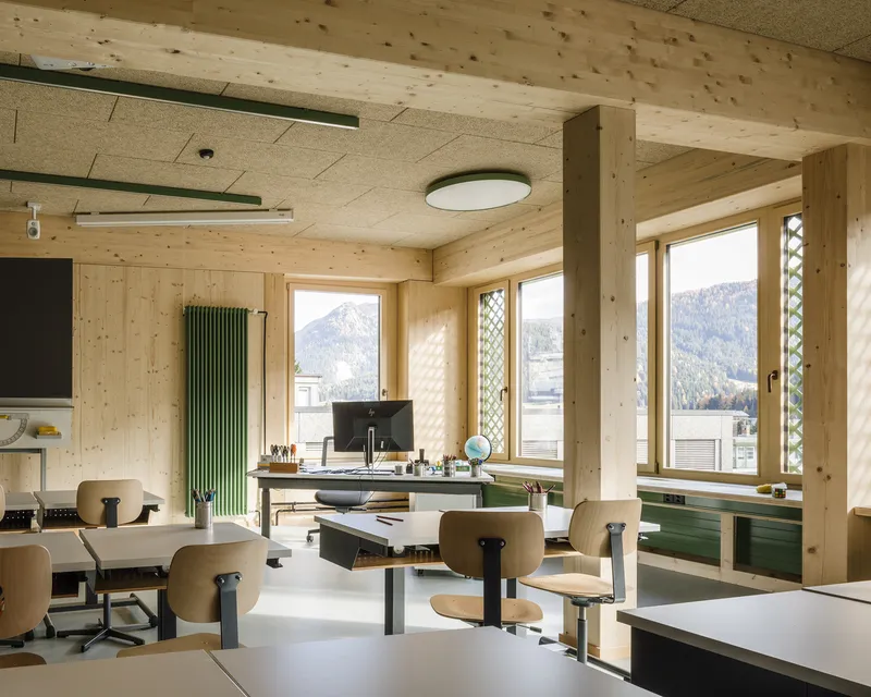 Classroom interior with exposed timber walls, ceiling, and windows framing mountain views in bright daylight