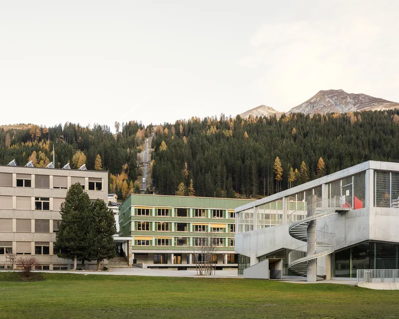 Campus view showing the green corrugated volume alongside concrete structures with curved external staircases