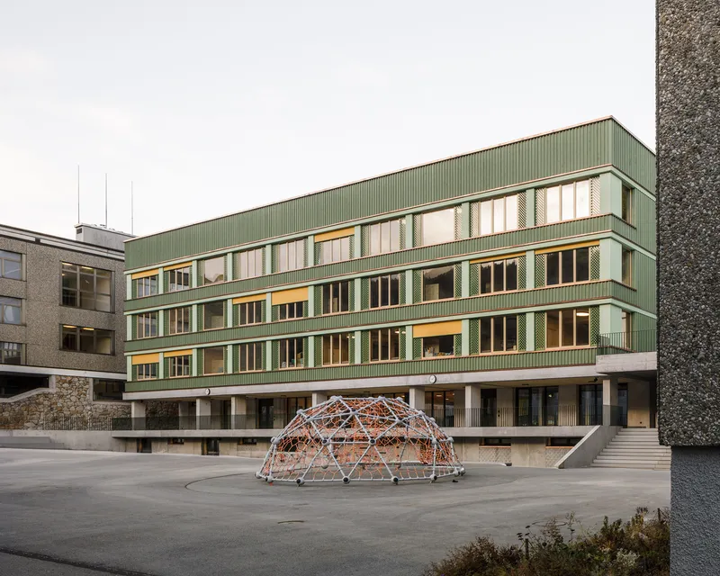 Green corrugated metal facade overlooking a concrete courtyard with a geodesic dome climbing structure