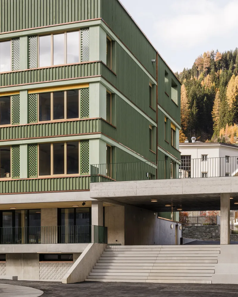 Concrete entry stairs leading to the elevated base beneath green corrugated cladding with forest beyond