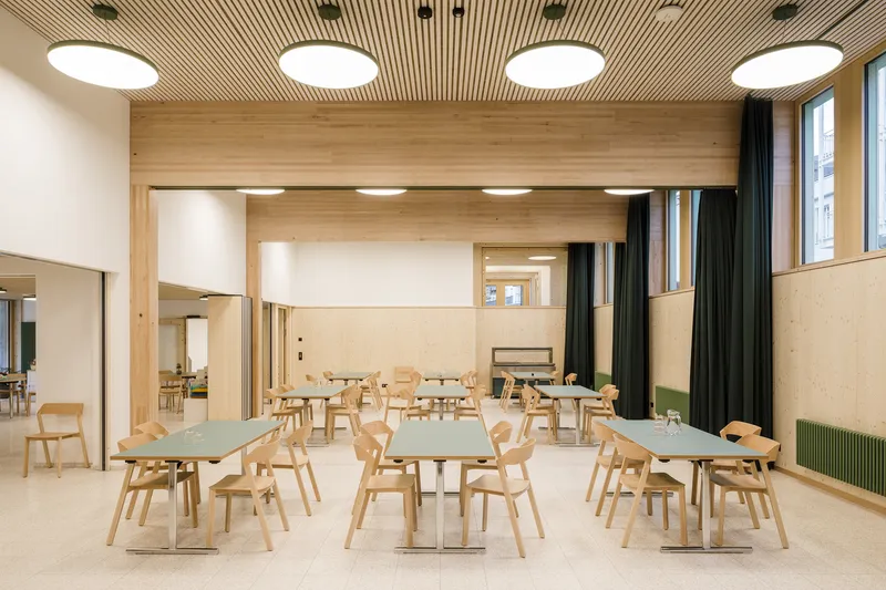 Light wood dining hall with terrazzo flooring and circular ceiling lights recessed in slatted timber