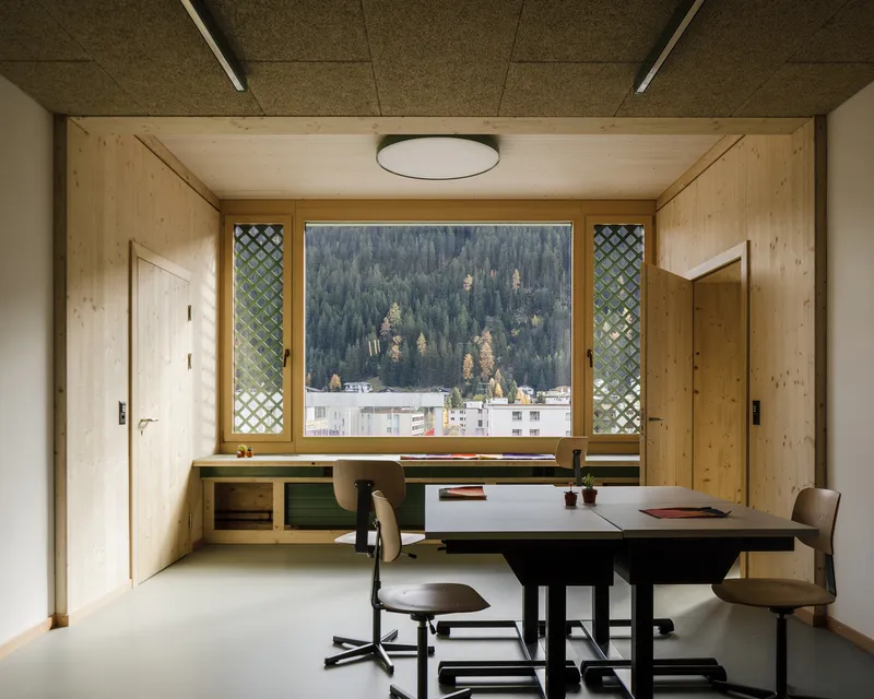 Classroom window seat framed by latticed sidelights overlooking forested hillside in autumn