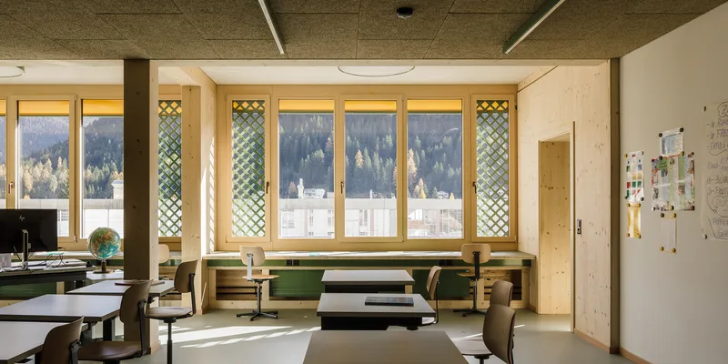 Office space with timber desks and latticed window panels framing snowy forested slopes beyond