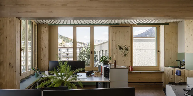 Open workspace with exposed pine walls and large windows overlooking rooftops and mountains in winter