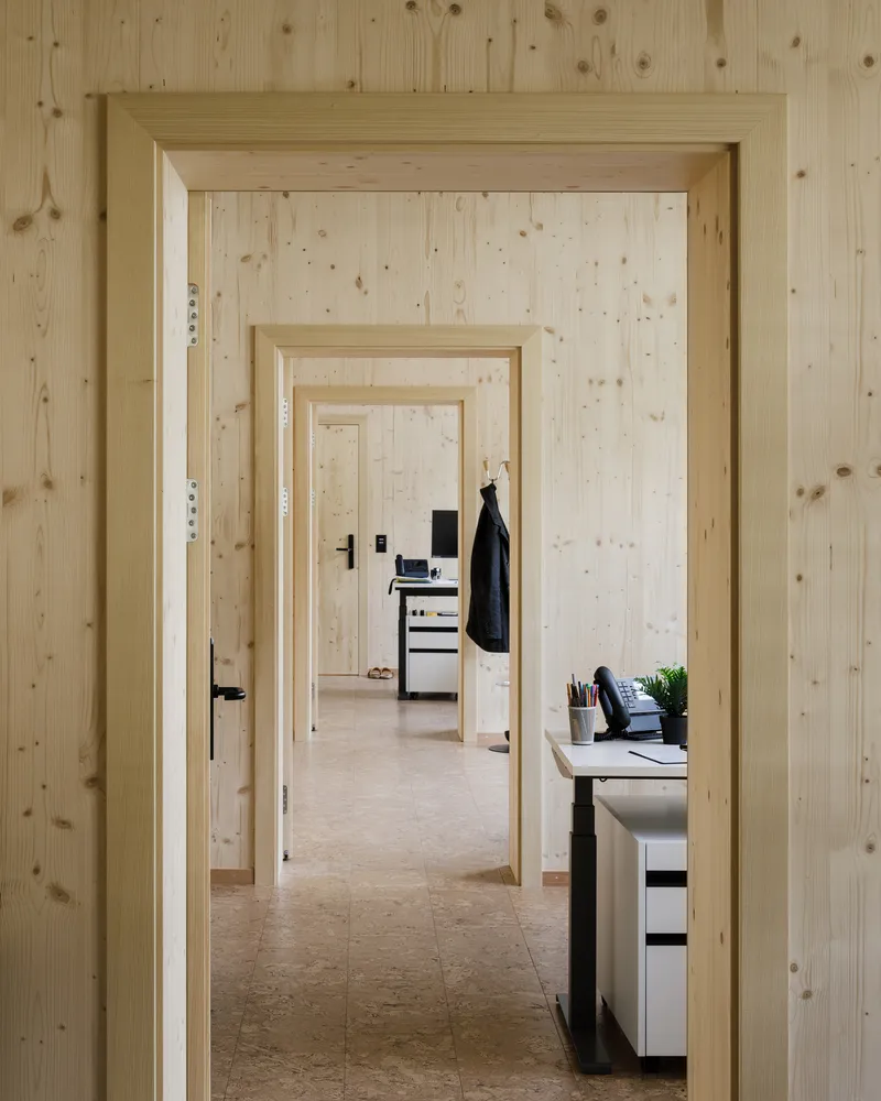Sequence of doorways through pine-clad walls revealing receding office rooms with a coat hanging visible