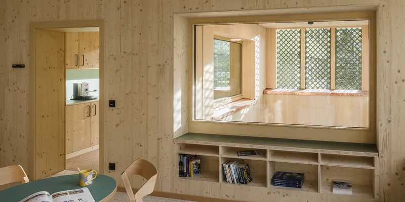 Built-in window seat with latticed panels and open shelving beneath in a pine-paneled room