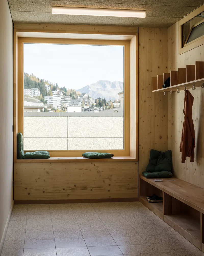 Entry nook with timber bench and coat hooks beside a large window overlooking a snow-dusted town