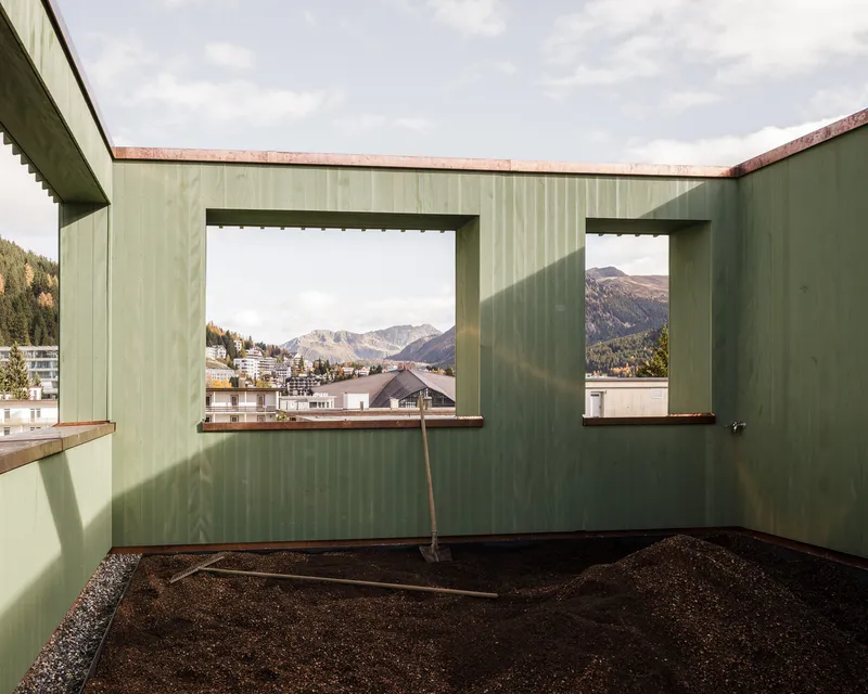Rooftop terrace with pale green panels and large openings framing mountain views under cloudy skies