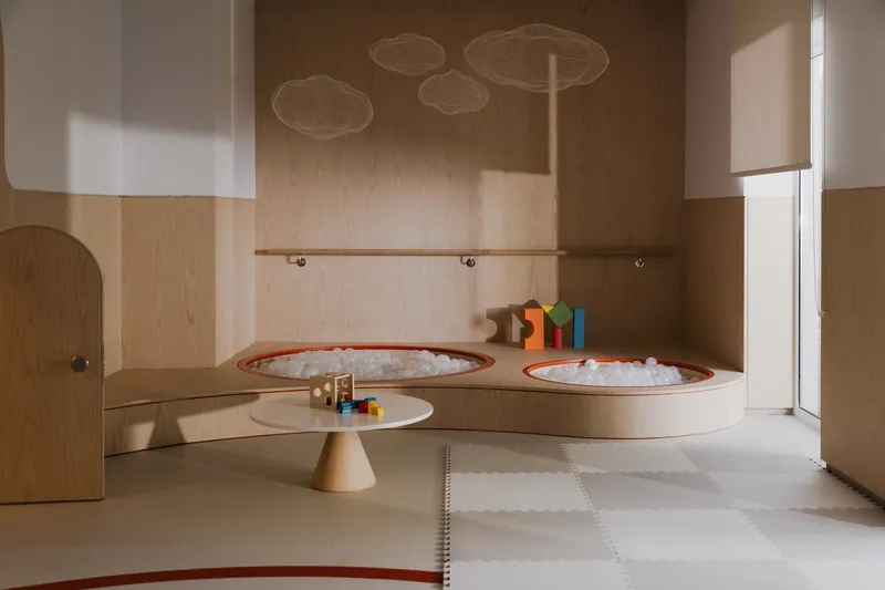 Interior play room with plywood walls, circular ball pits with orange trim, and mesh cloud fixtures suspended above
