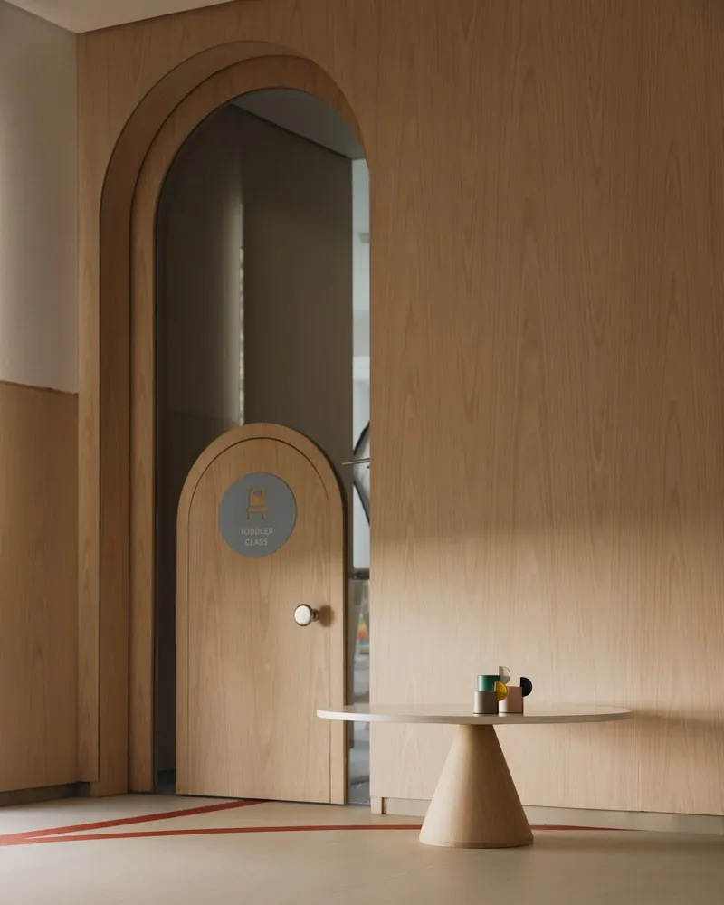 Close-up of arched plywood doorway with circular signage and conical table in soft natural light