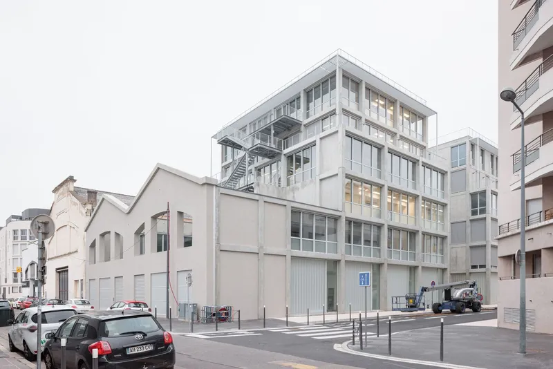 Street view of the pale concrete and glass facade with external steel staircase under an overcast sky