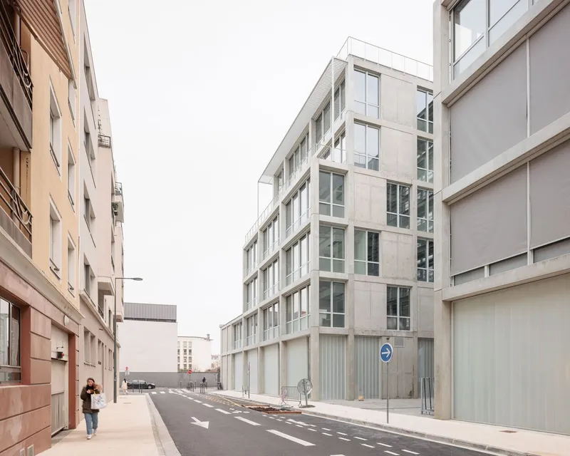 Corner view of the concrete and glass facade with a pedestrian walking along the narrow street