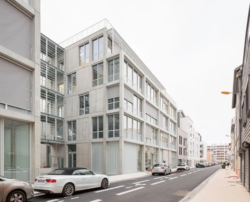 Streetscape showing the concrete panel facade with recessed ground floor and parked cars along the curb