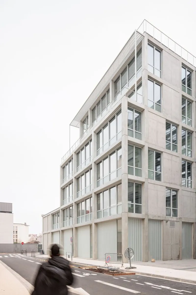 Street view of the staggered facade with concrete base and glazed upper floors as a cyclist passes