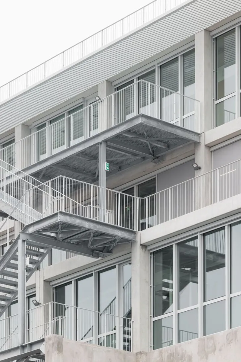 Stacked balconies with white metal railings and diagonal stair runs beneath corrugated cladding