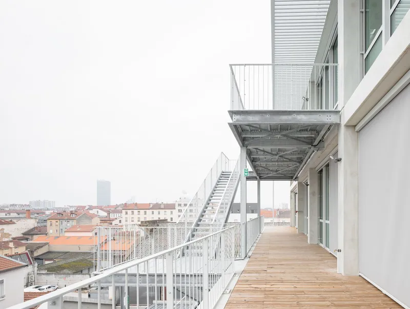Timber deck balcony with metal railing overlooking rooftops under an overcast sky