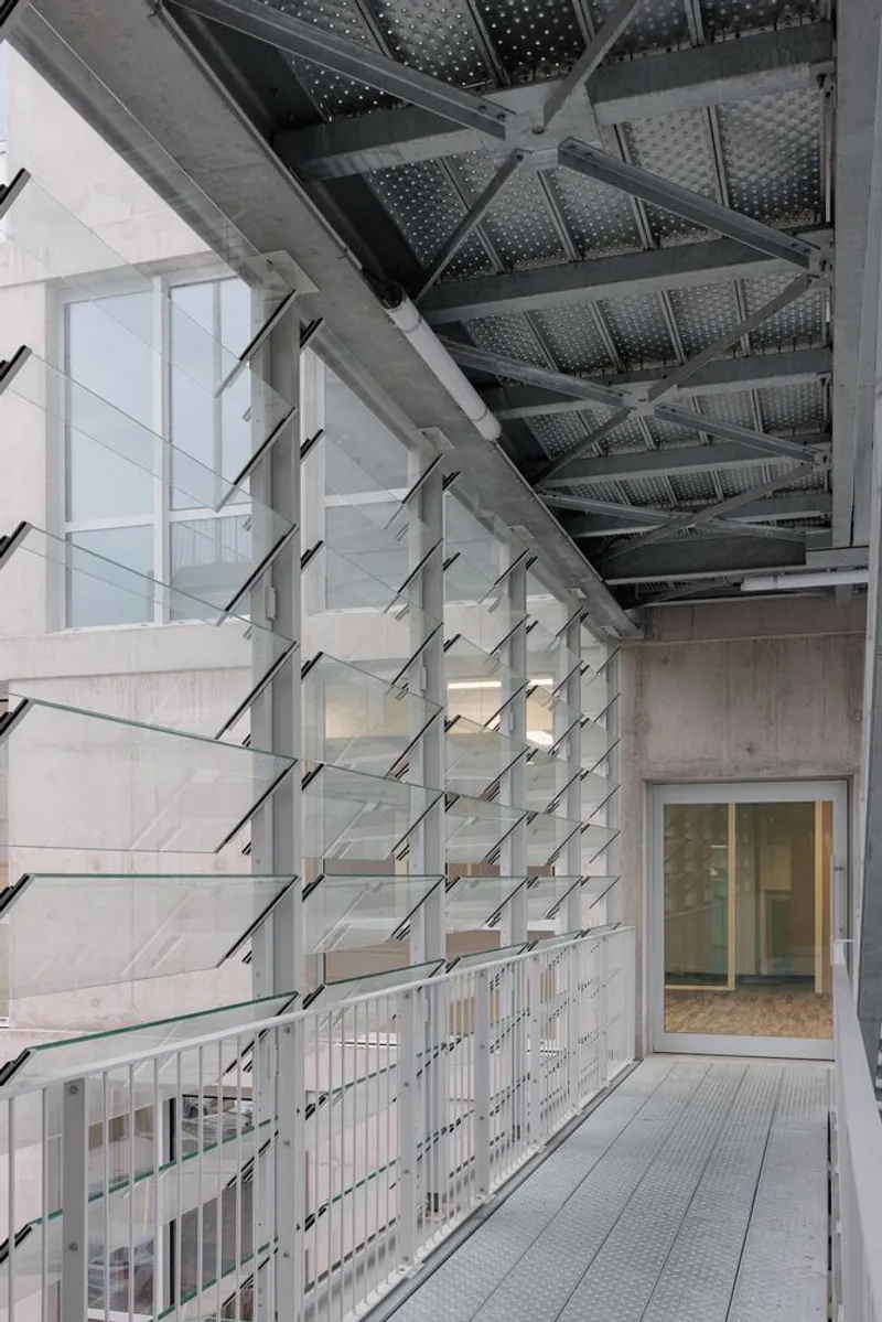 Perforated steel underside of balcony above hinged glass louvres and concrete corridor