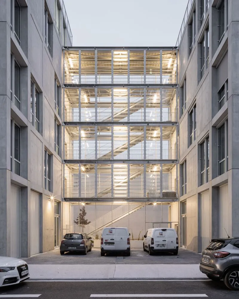 Interior courtyard with a glass-enclosed stairwell connecting floors above parked vehicles at dusk