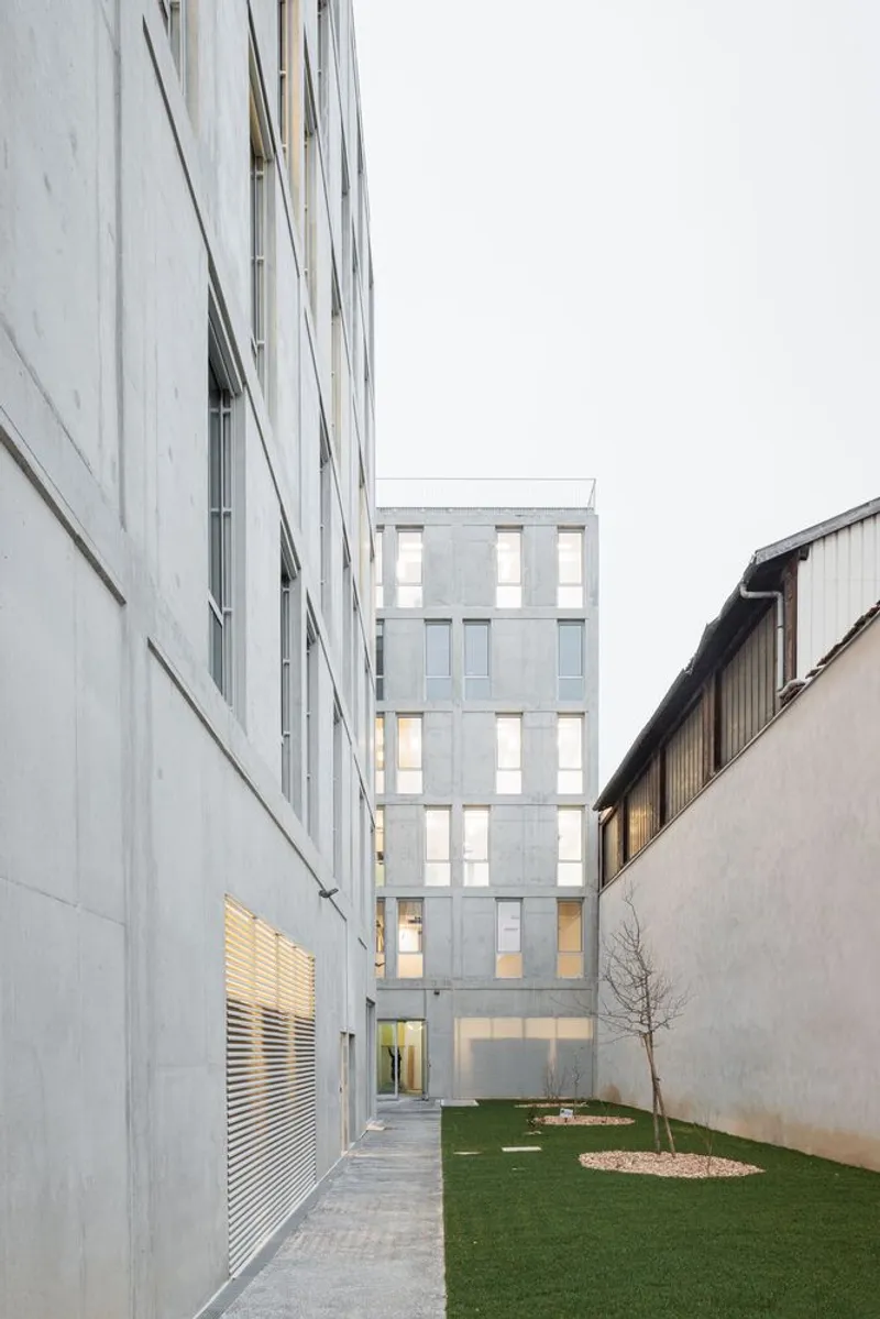 Courtyard view showing the rear facade with illuminated windows and a small grass lawn at dusk
