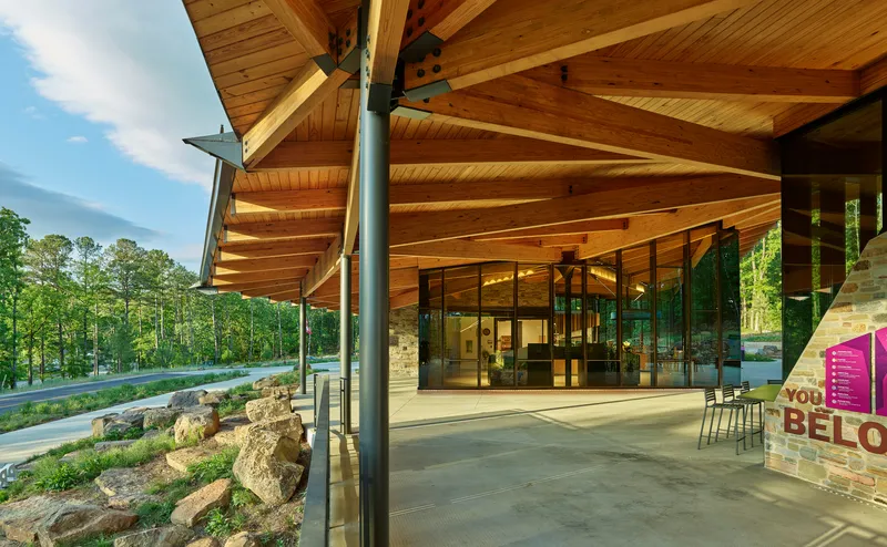 Covered entry terrace with sloping timber soffit, steel column, and view toward glass entrance doors