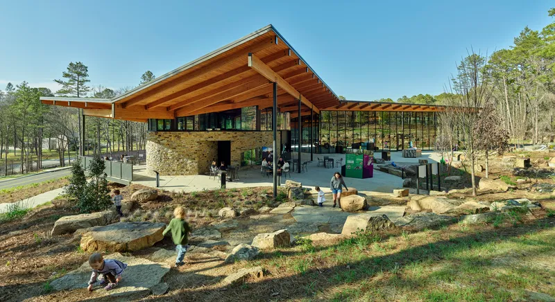 Open-air pavilion with exposed timber beams and stone core overlooking a natural play area with children