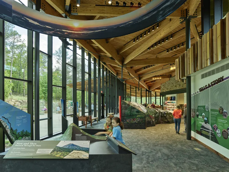 Exhibition hall with radial timber ceiling beams and educational displays along a corridor of glass and steel