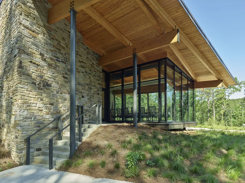 Exterior staircase with metal railings ascending alongside a stacked stone wall toward the glass pavilion entry