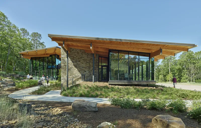 Dual pavilions with overhanging timber roofs connected by pathways through planted beds and scattered boulders
