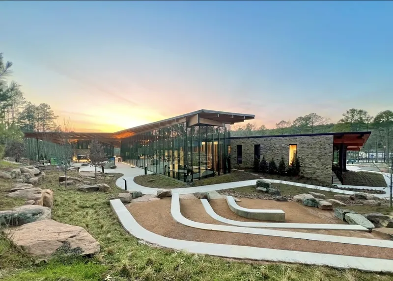 Cantilevered roof with exposed timber beams over glass walls and stone volumes at sunset