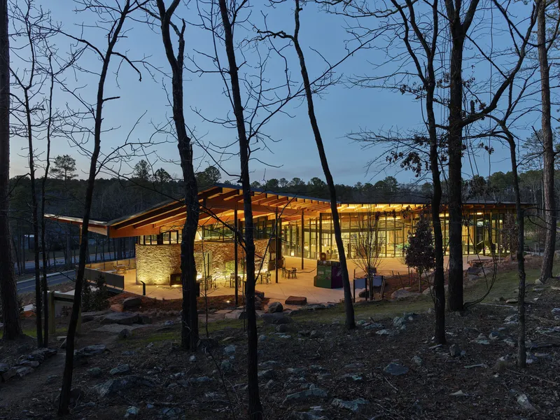 Glazed pavilion with timber roof framed by bare trees in the evening light